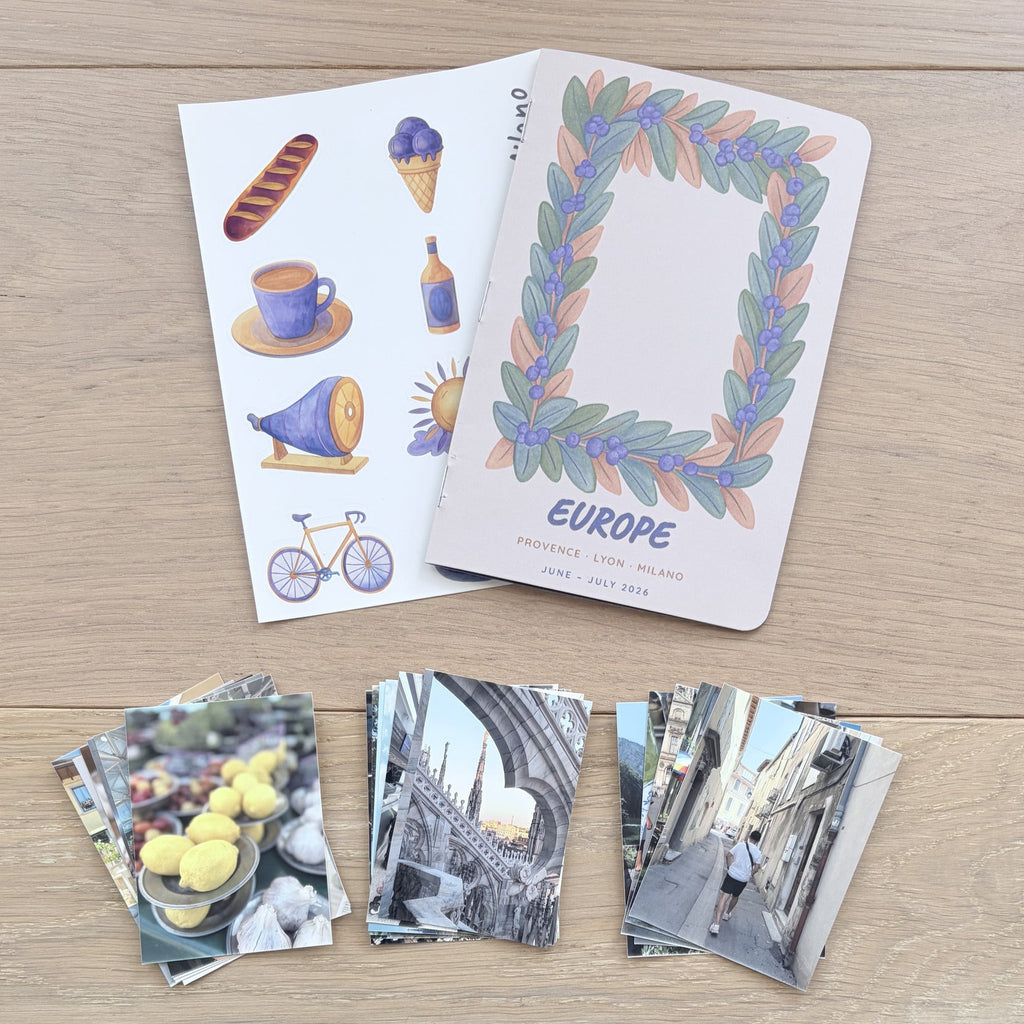 A set of Europe-themed travel cards and matching photo prints arranged on a light wood tabletop. The cards feature illustrated motifs like a bicycle, coffee cup, and bread, with one card displaying a colorful leaf wreath border and the word 'EUROPE'.